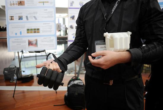 person shows off prosthetic hand with research poster in background